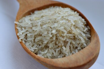 White rice in a wooden spoon on white background, close-up — concept of natural nutrition, visual purity and culinary simplicity for healthy lifestyle