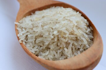 White rice in a wooden spoon on white background, close-up — concept of natural nutrition, visual purity and culinary simplicity for healthy lifestyle