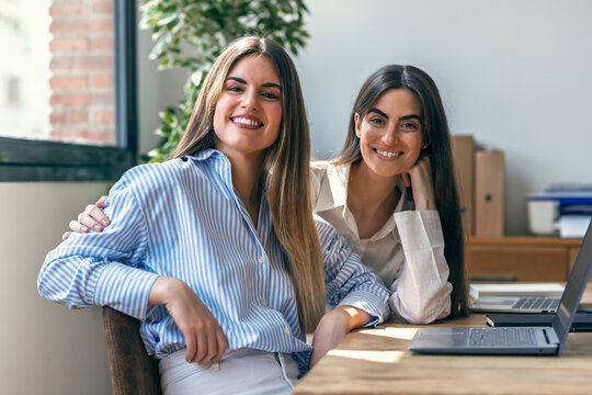 Two beautiful designer women working together with laptop while looking at camera in the office - Powered by Adobe