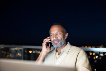 Focused young businessman working late at night in office with laptop and mobile phone