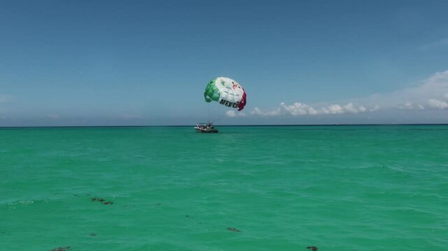 Paraca&iacute;das con los colores de la bandera de mexico levantando el vuelo sobre el mar caribe.