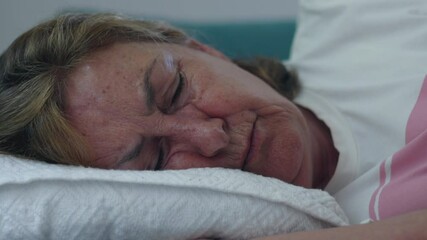 Close-up of elderly woman sleeping with head on white pillow, eyes closed and face calm, moment of deep rest and quiet in domestic setting
