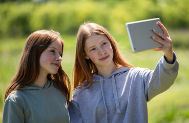 Twins taking a photo on tablet while in a field