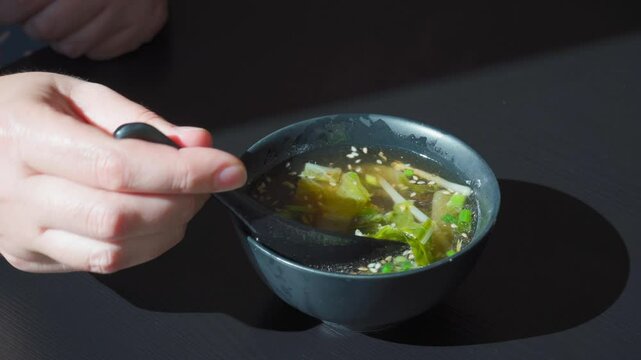 Eating fish broth with greens, sesame seeds and herbs, clear broth, shio ramen, salmon bouillon, japanese soup in black bowls