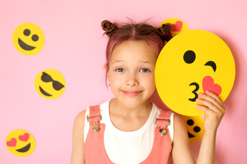 A cute little child holds a smile face depicting a kiss. World Emoji Day on July 17th