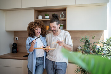 Couple eating sushi in modern kitchen using chopsticks