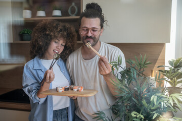 Happy couple eating sushi with chopsticks in modern kitchen