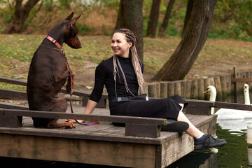 Woman sitting on dock with Doberman dog near scenic lake view