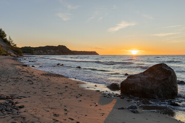 a large rock on a picturesque beach is washed by the sea at sunset
