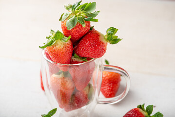 Strawberries in a mug, a glass mug with beautiful strawberries on a white rustic wooden surface, abstract background, selective focus.
