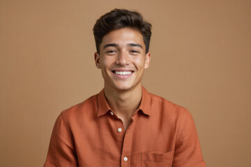 Obraz premium A young man with dark hair and a warm smile gazes directly at the camera, wearing a casual orange shirt against a solid brown background.