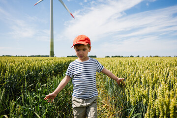 Child walking through a golden wheat field, surrounded by tall crops and a wind turbine, enjoying a...