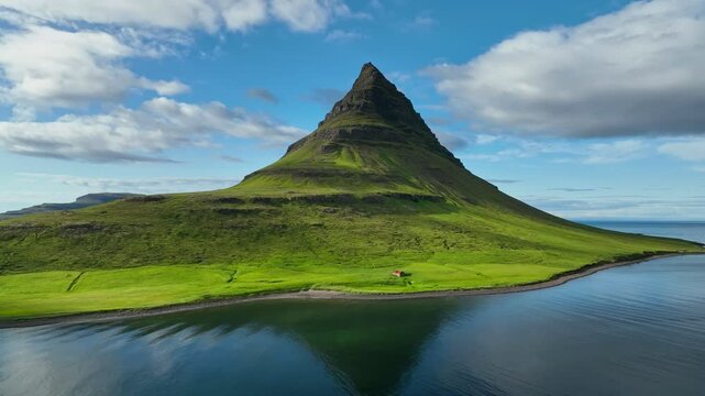 Flying around epic green mountain in Iceland - Kirkjufell - Church Mountain. Pointed green mountain on the coast and small house at its foot - one of the most famous view in Iceland