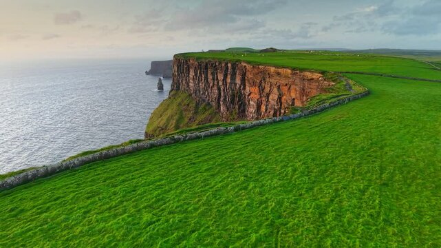 Flying over green grass near the edge of Cliff of Moher - one of the most popular tourist destinations in Ireland. Aerial breathtaking cliffs of Moher in Ireland, County Clare