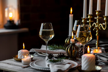 Beautiful table setting for family Christmas dinner at home. Cozy atmosphere, candlelight. Wine glasses, vintage chandelier, elegant interior. Fir tree branches, wooden furniture, dark, bokeh