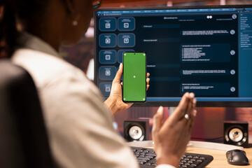 Woman seated at desk using AI LLM chatbot software and green screen phone in modern urban home...