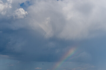 Clouds gather in the sky creating a beautiful rainbow after the rain near a serene landscape in the afternoon