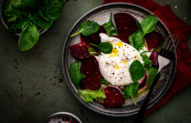 Gourmet salad with burrata cheese, baked beets, spinach and olive oil, green stone background, top view