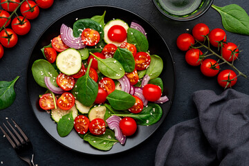 Healthy salad with spinach, tomatoes, cucumber, onion, sesame and olive oil, top view