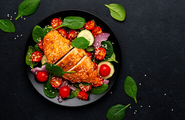 Healthy vegetable salad with grilled chicken, spinach, tomatoes, cucumber and red onion. Black table background, top view