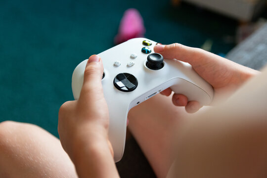 A child is holding a wireless white gaming console gamepad. Close-up view with blurred background