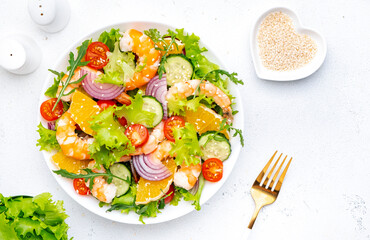 Gourmet seafood salad with big shrimp, orange slices, fresh lettuce, cherry tomatoes, cucumbers, onion and sesame, top view