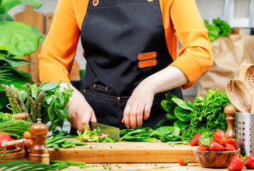 Chef woman in apron skillfully prepares fresh vegetables on a wooden cutting board in a bright...