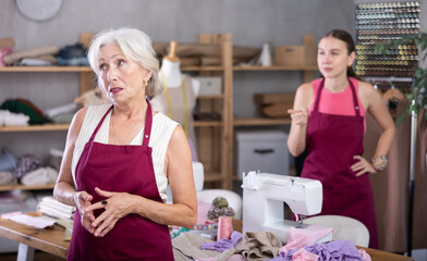 Adult female seamstress scolding elderly woman assistant in sewing workshop