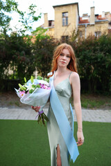 Teen girl in green formal dress smiling with sash and fresh flowers.