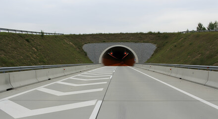 Road Tunnel Entrance On The Highway Ahead Underneath A Green Grassy Mound