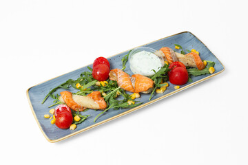 Red fish skewers with tomatoes, arugula, corn, and tartar sauce on a plate against a white background