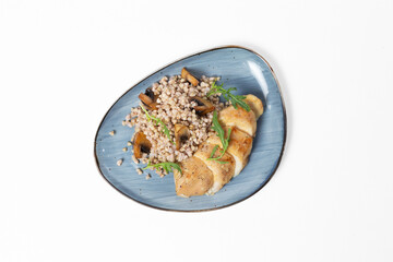 Buckwheat with sautéed mushrooms and baked chicken fillet on a plate against a white background