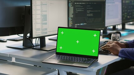 Employees using green screen laptop, working in server farm to optimize it for data processing requirements. Close up of mockup notebook on desk next to workers coding in data center, camera A