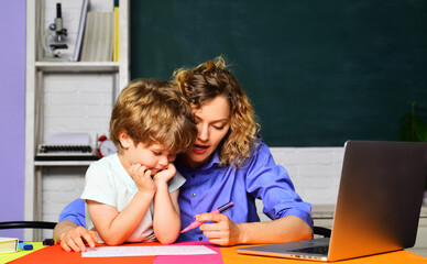 Female elementary school teacher helping cute schoolboy with homework. Knowledge, education and...