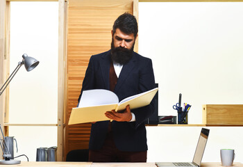 Businessman standing at table holding folder with documents working in office. Bearded man in suit...