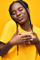 A joyful young woman of African descent wearing a bright yellow t shirt, holding a fresh burger...