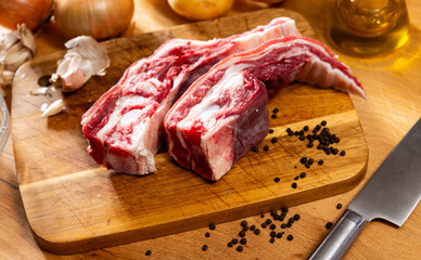 Fresh raw pork ribs with potatoes, onions and black pepper on wooden table in kitchen