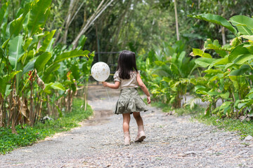 Latina toddler mid-step runs down pebbled zoo trail clutching white balloon surrounded by greenery.