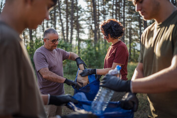 family of volunteers men woman pick up waste garbage to clean forest
