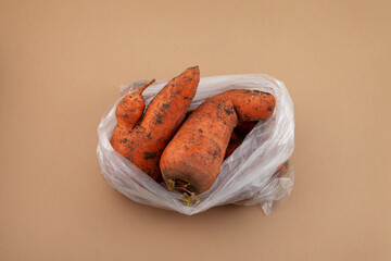 Ugly vegetables. Carrots with flaws in plastic bag on beige background. Concept - Food waste...