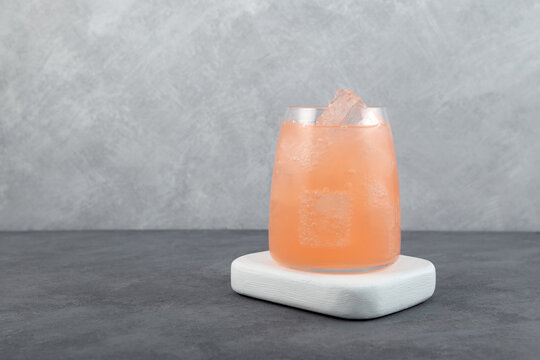 Pink cold summer cocktail in glass cup. Refreshing cold grapefruit gin tonic drink with ice cubes. Delicious iced beverage