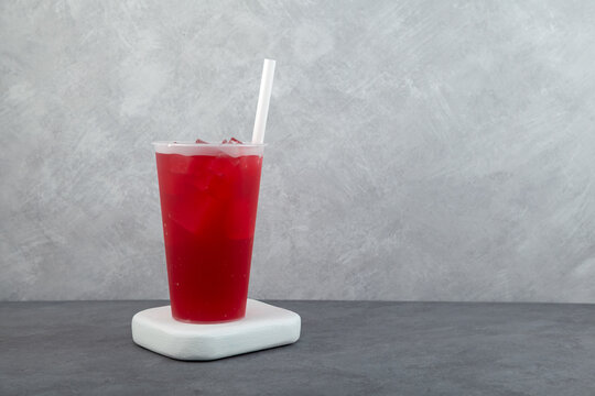 Red iced hibiscus drink in plastic cup with drinking straw. Glass of Karkade ice tea, take away beverage. Jamaica drink or Agua de Jamaica. Refreshing summer iced drink. Rose cold cocktail