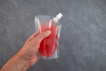 Man's hand holds an airtight doy pack for drinks. Red drink for adults or wine slushy in plastic...