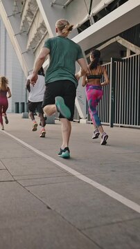 Back view of multiethnic team of men and women training running before marathon, active life. Running club, group of like-minded people run early in the morning at dawn along the urban streets
