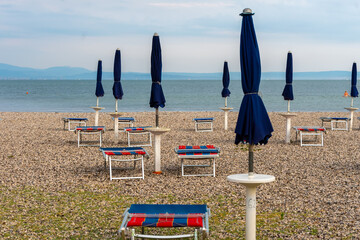 Empty pebble beach with covered blue umbrellas and sunbeds in the morning.
