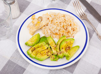 Healthy satisfying dinner option featuring boiled creamy basmati rice with chicken breast and sliced soft avocado sprinkled with sesame seeds served on white plate