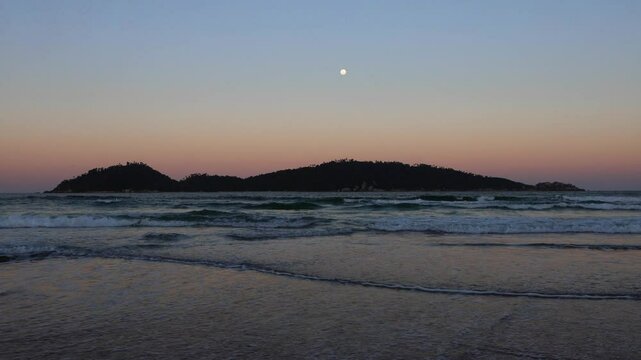 waves crashing on tropical beach with full moon over island in background