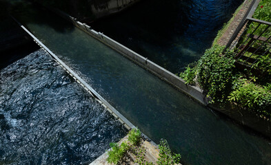 View from above of a narrow river flowing over a bridge over another canal. Green plants grow next to the water.