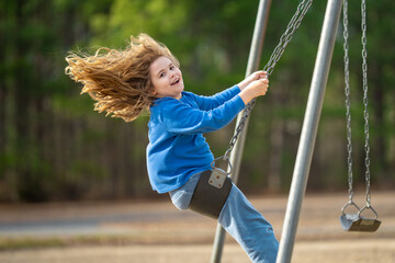 Playful child on swing in park. Little kid with blond hair on a swing. Smiling happy kid on swing....