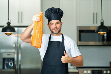 Chef with raw meat fish salmon fillet on kitchen. Chef man in uniform on kitchen. Handsome man chef...
